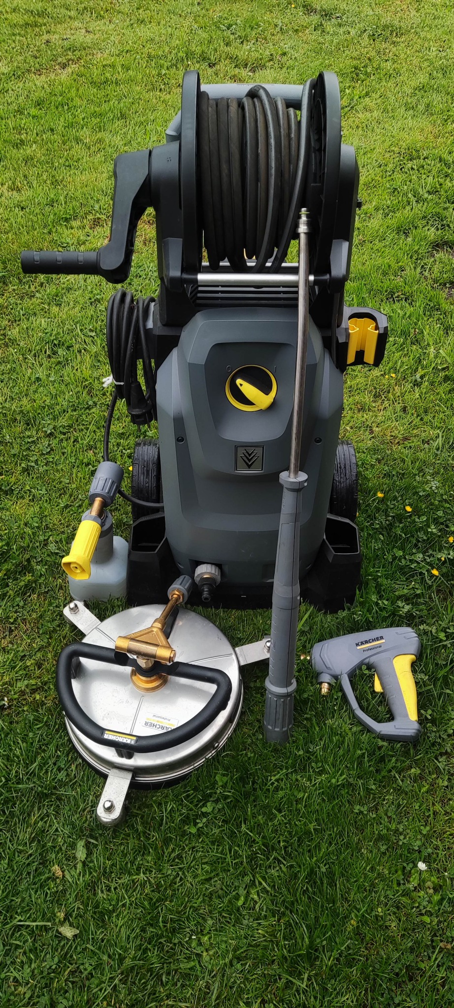 Profesjonalna myjka ciśnieniowa Kärcher z akcesoriami na trawie: lanca, dysza rotacyjna i przystawka do powierzchni płaskich, gotowa do użycia.