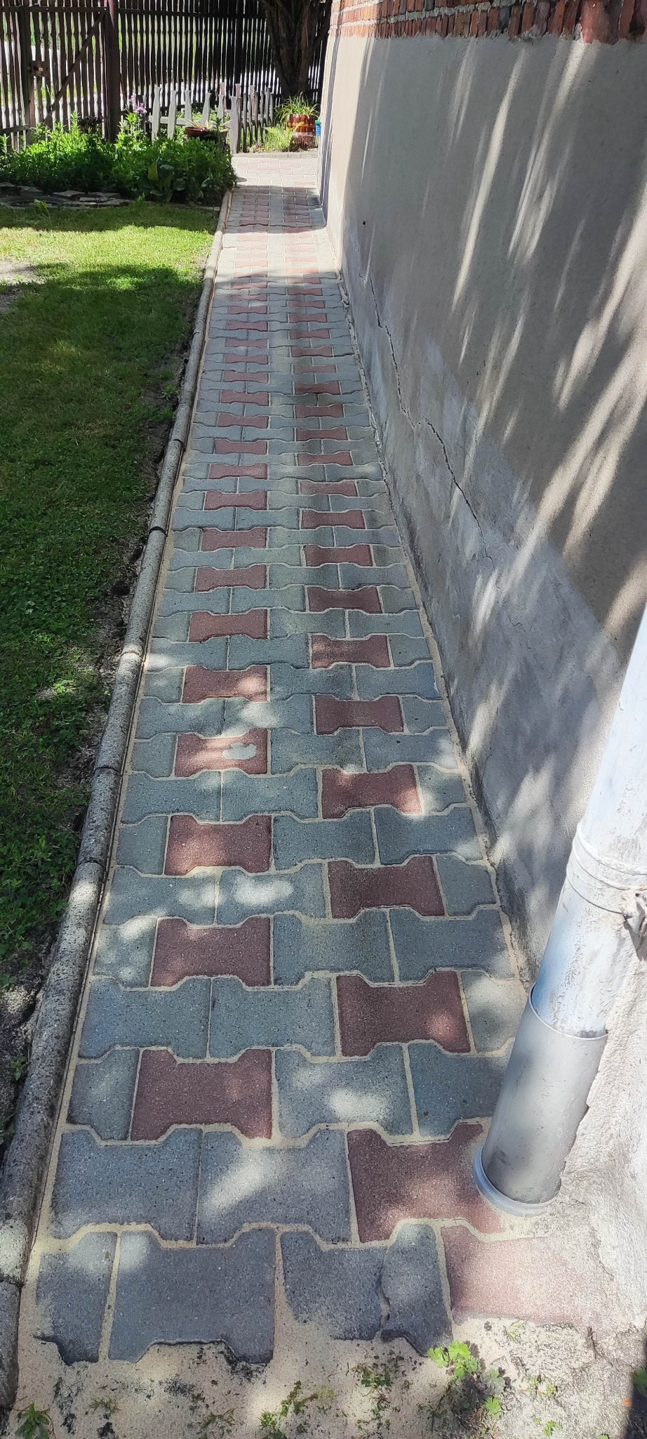 Świeżo ułożona, dwukolorowa kostka brukowa w odcieniach szarości i czerwieni, z widocznymi resztkami piasku na powierzchni spoin, przylegająca do szarej ściany budynku.