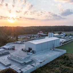 Marcin Czarnowski Firma Usługowo-Handlowa - Fabryka prefabrykatów betonowych z placem składowym pełnym ułożonych płyt. Widok z lotu ptaka, zachód słońca w tle.