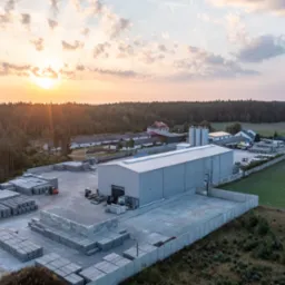 Fabryka prefabrykatów betonowych z placem składowym pełnym ułożonych płyt. Widok z lotu ptaka, zachód słońca w tle.
