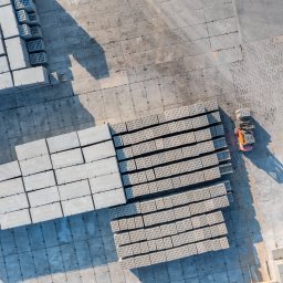 Marcin Czarnowski Firma Usługowo-Handlowa - Widok z góry na plac składowy z ułożonymi prefabrykatami betonowymi i wózkiem widłowym. Silne cienie podkreślają strukturę i wzór ułożenia elementów.