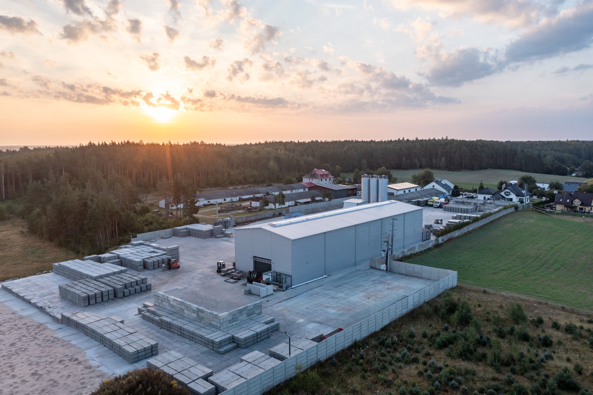 Fabryka prefabrykatów betonowych z placem składowym pełnym ułożonych płyt. Widok z lotu ptaka, zachód słońca w tle.