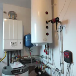 Biały piec Immergas z szarym zbiornikiem, niebieskim naczyniem wzbiorczym i białym zasobnikiem ciepłej wody, uzupełnione instalacją, widok z bliska.