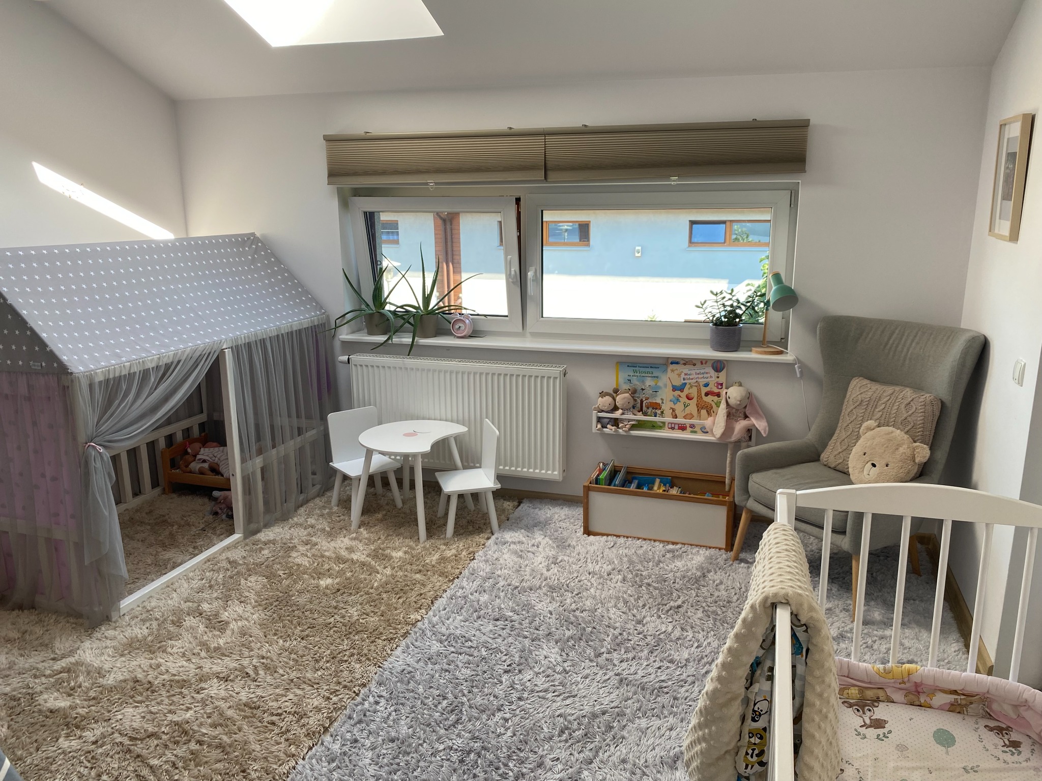 Jasny pokój dziecięcy z baldachimem w gwiazdki, białym stolikiem i krzesłami, pluszowymi zabawkami i łóżeczkiem. Dywan w odcieniach beżu i szarości.