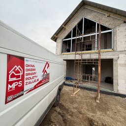 MPS-OKNO DOM KATARZYNA SZKUTNIK - Montaż okien w surowym budynku z rusztowaniem. Na pierwszym planie samochód dostawczy z reklamą firmy MPS Okno-Dom z Janowa Lubelskiego.