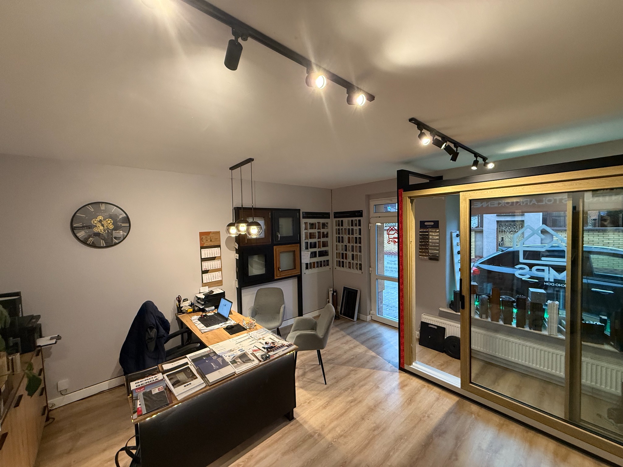 Salon sprzedaży okien i drzwi z ekspozycją przesuwnych konstrukcji, biurkiem z katalogami i wzornikami, oświetleniem punktowym.