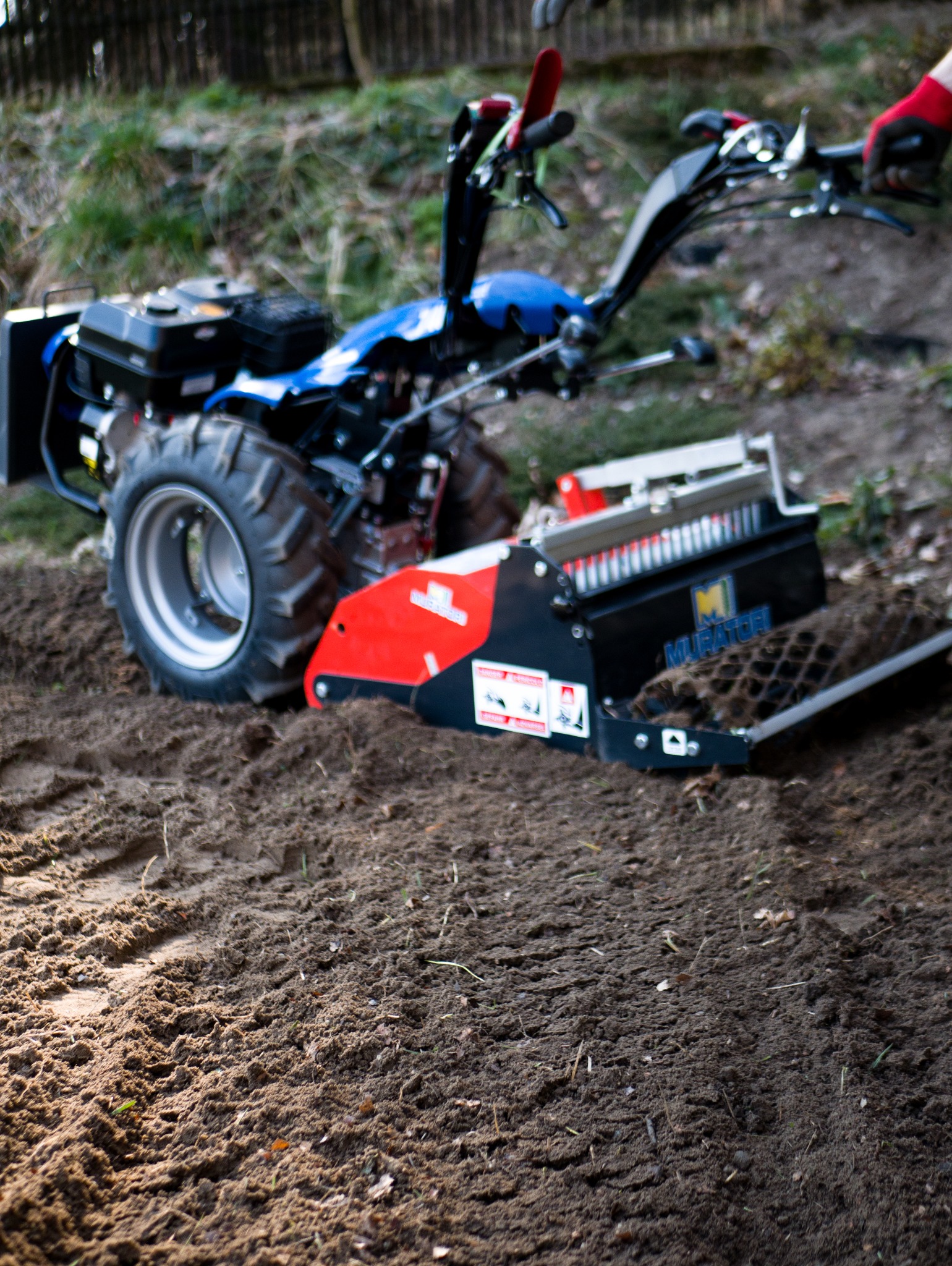 Głębosz glebowy w trakcie pracy, spulchniający ziemię pod przyszły ogród. Widoczne ślady na ziemi, maszyna z bliska, czerwone elementy. Przygotowanie gleby.