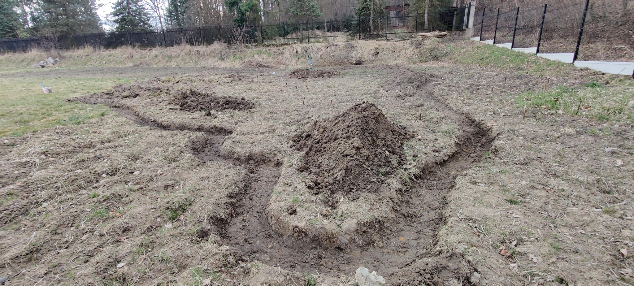 Przygotowanie terenu pod ogród: wykopane rowy i pryzma ziemi na zaniedbanym trawniku. Widoczne paliki wyznaczające granice rabat.