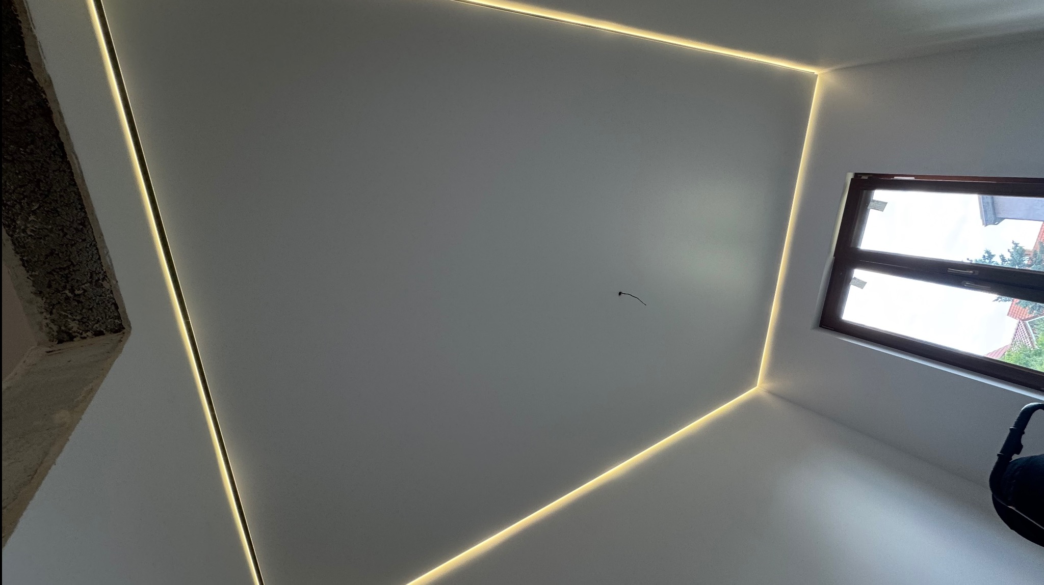 Biały sufit z subtelnym oświetleniem LED wzdłuż krawędzi, widok z dołu, okno w rogu. Minimalistyczny design wnętrza.