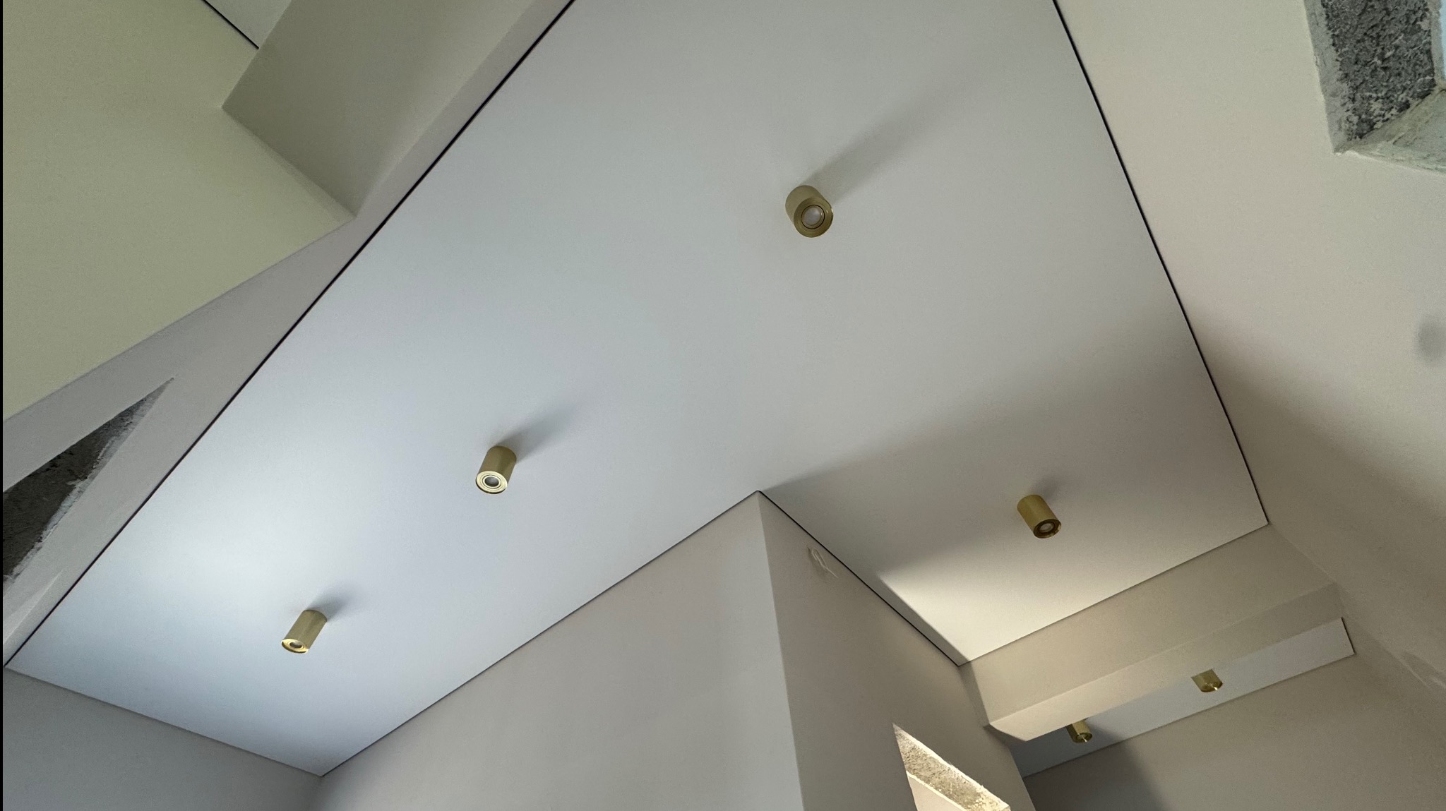 Biały sufit z precyzyjnie zamontowanymi, złotymi punktowymi lampami LED, podkreślającymi nowoczesny design wnętrza. Widok z dołu.