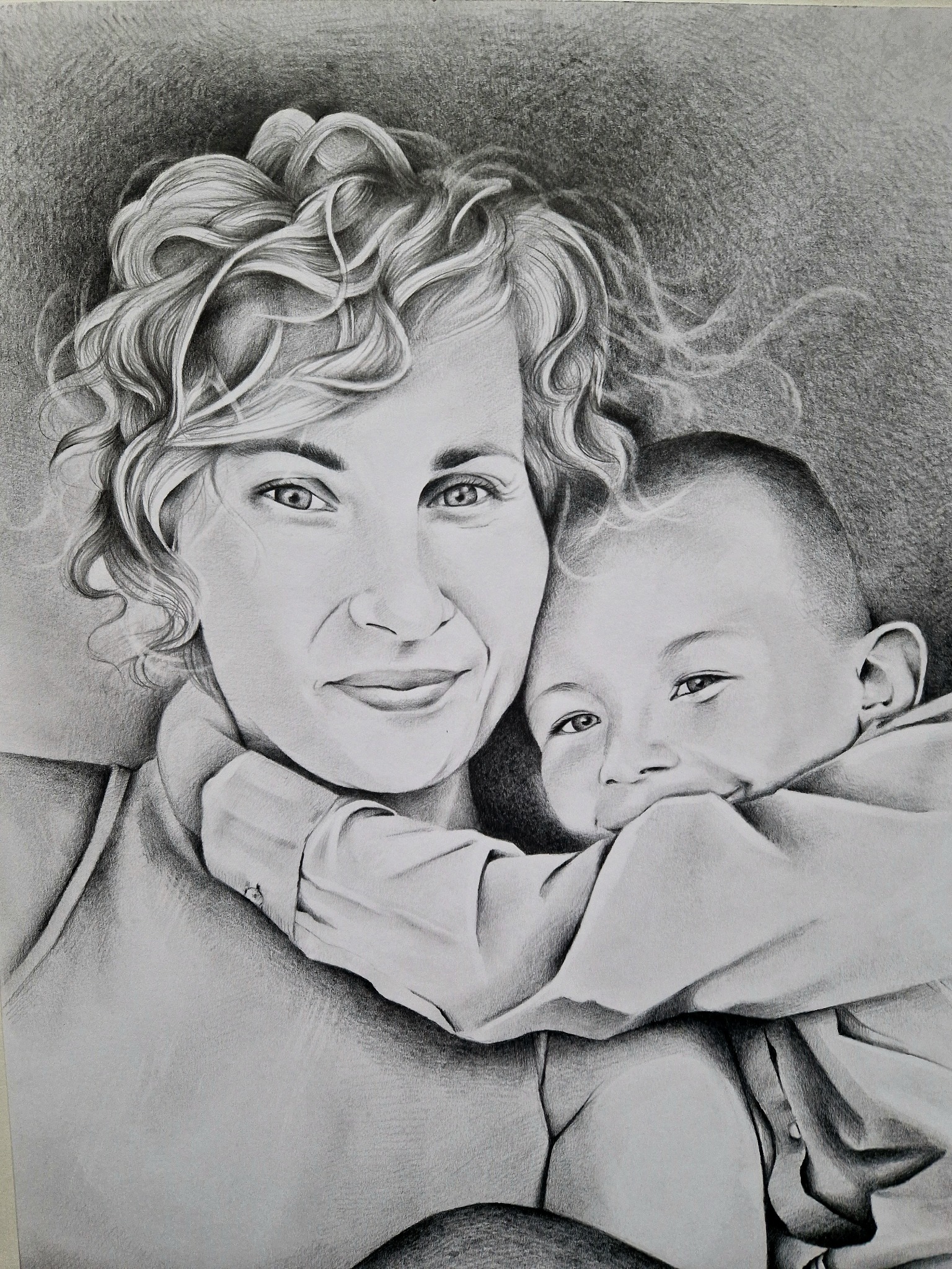 Ołówkowy portret matki z dzieckiem, wykonany z dbałością o detale włosów i rysów twarzy, z delikatnym cieniowaniem tła. Praca artystyczna, czarno-biała.