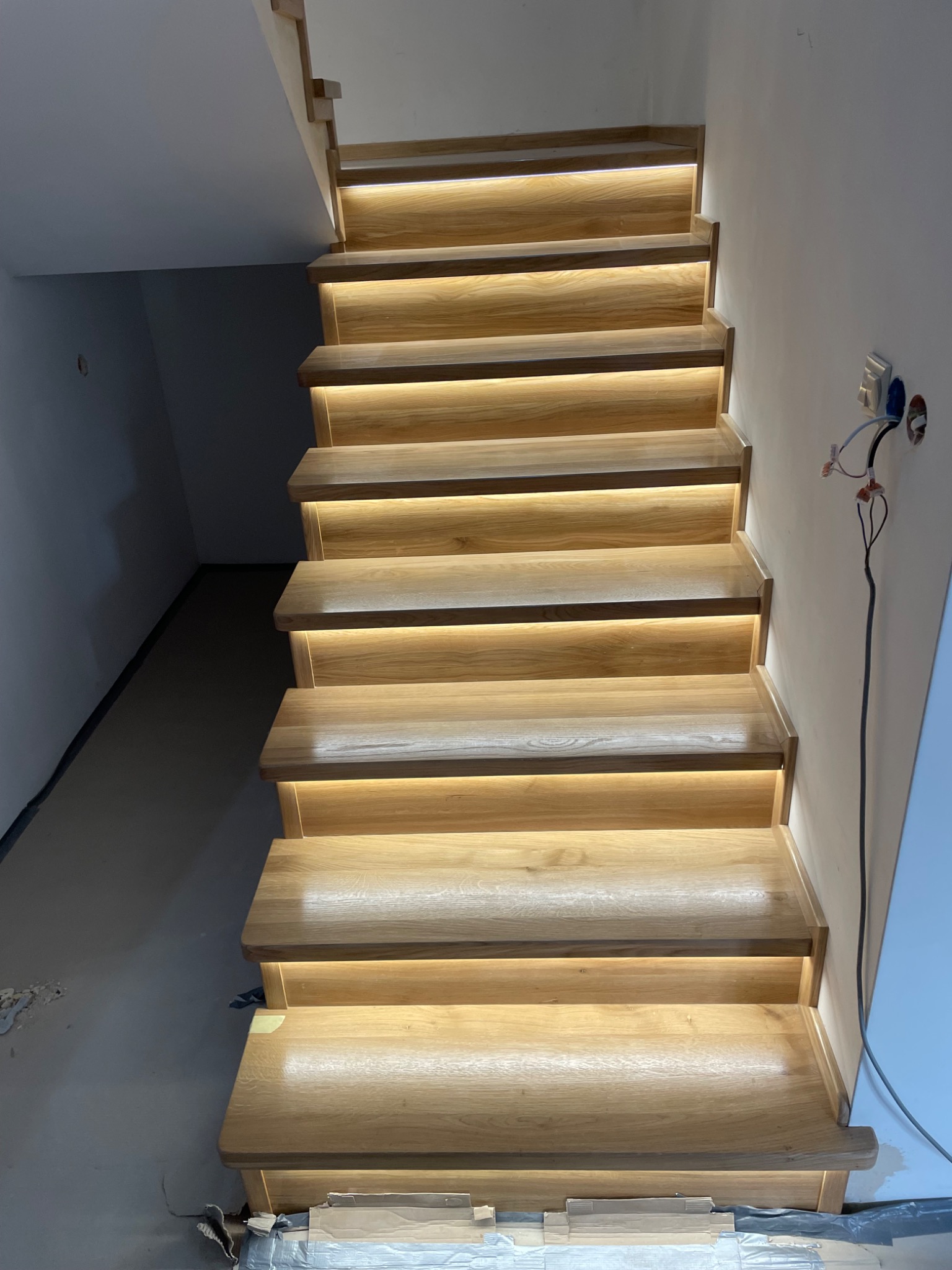 Drewniane schody z podświetleniem LED w Kłocku. Widok z dołu, ukazujący detale wykończenia i ciepłe światło. Nowoczesny design i solidne wykonanie.