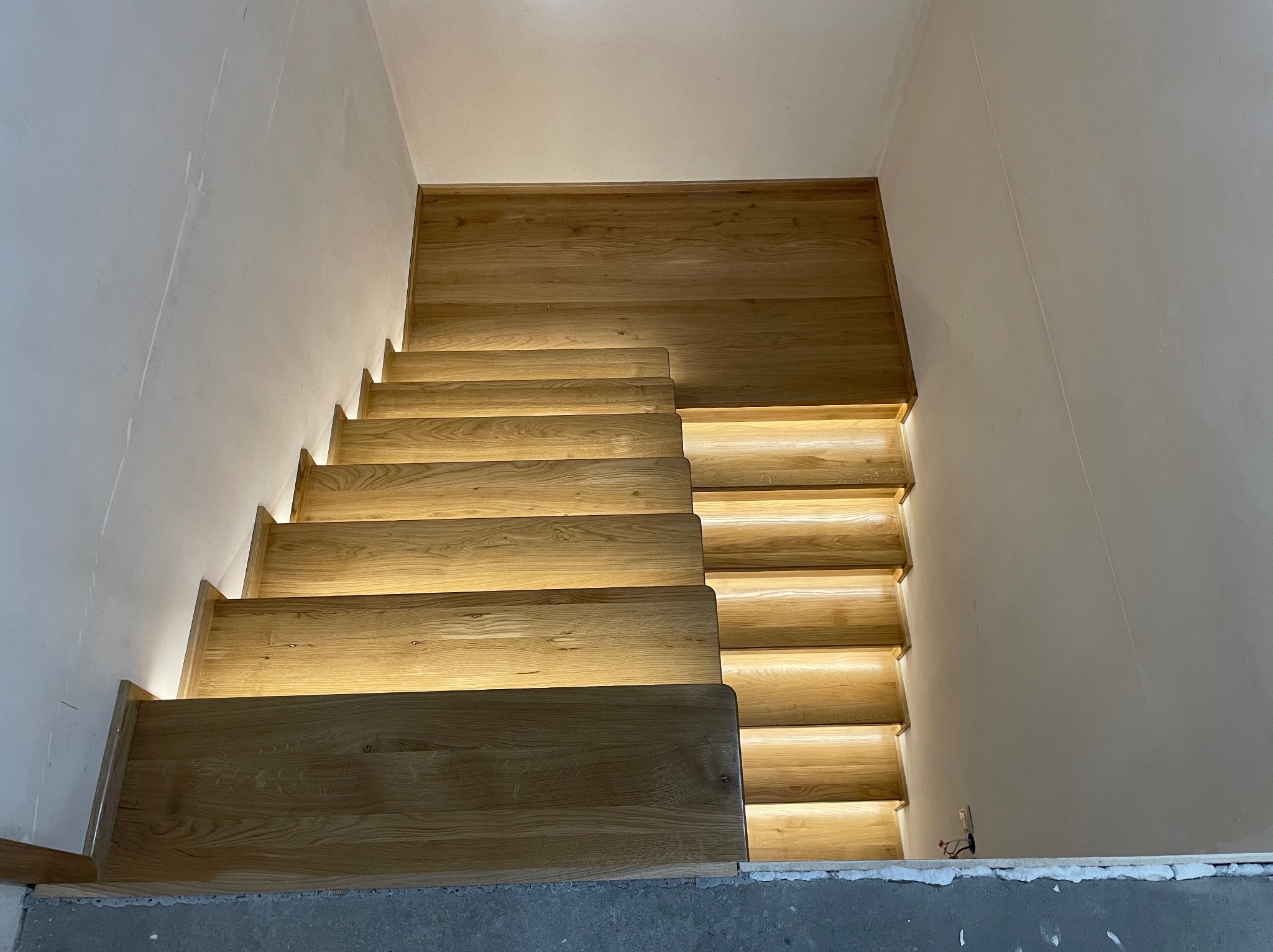Drewniane schody z podświetleniem LED, widok z dołu. Jasne drewno, nowoczesny design, białe ściany. Detal wykończenia wnętrza z subtelnym oświetleniem.