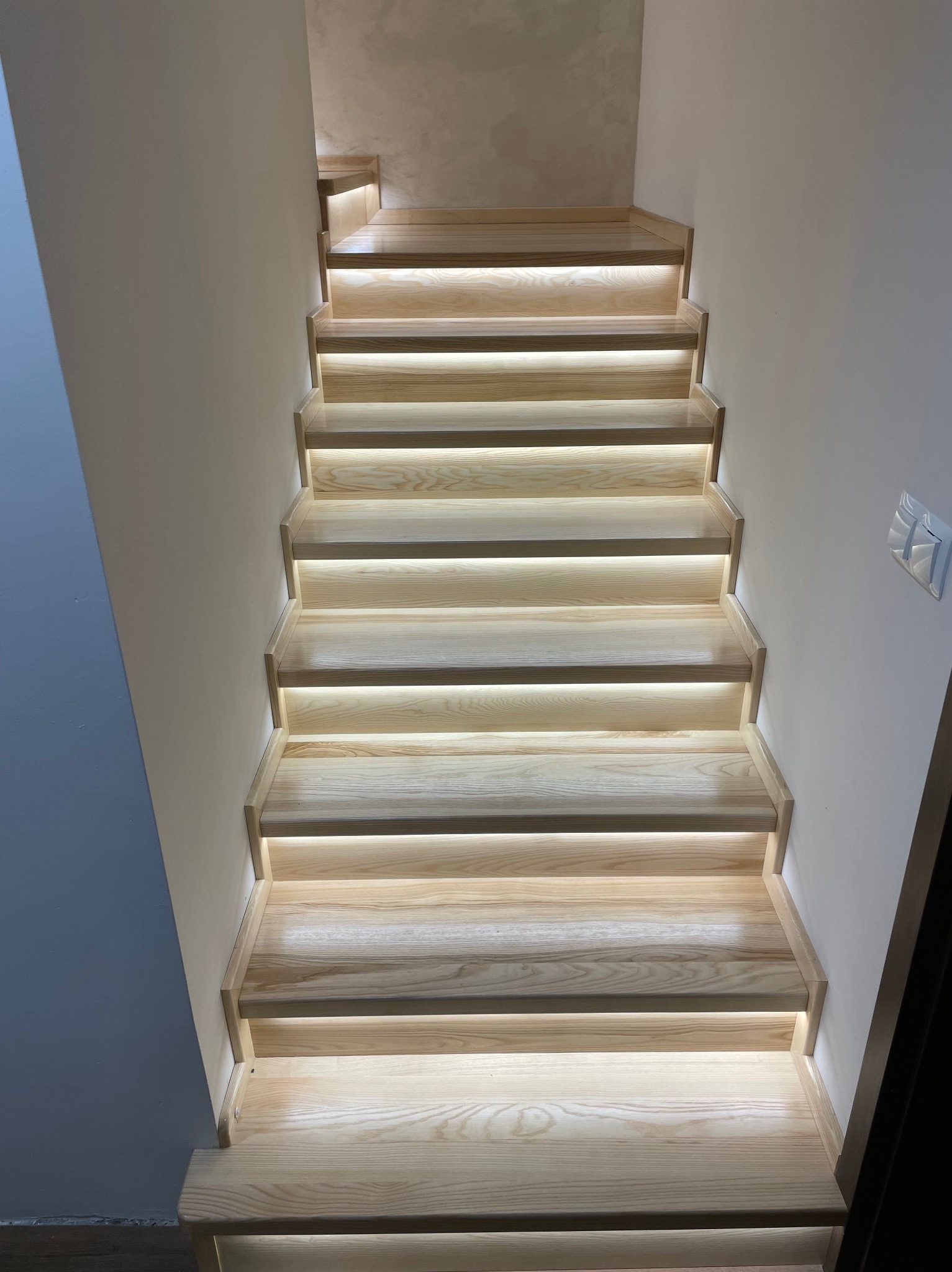 Drewniane schody z subtelnym oświetleniem LED, widok z dołu. Jasne drewno, minimalistyczny design, ciepłe światło tworzy nowoczesny klimat.