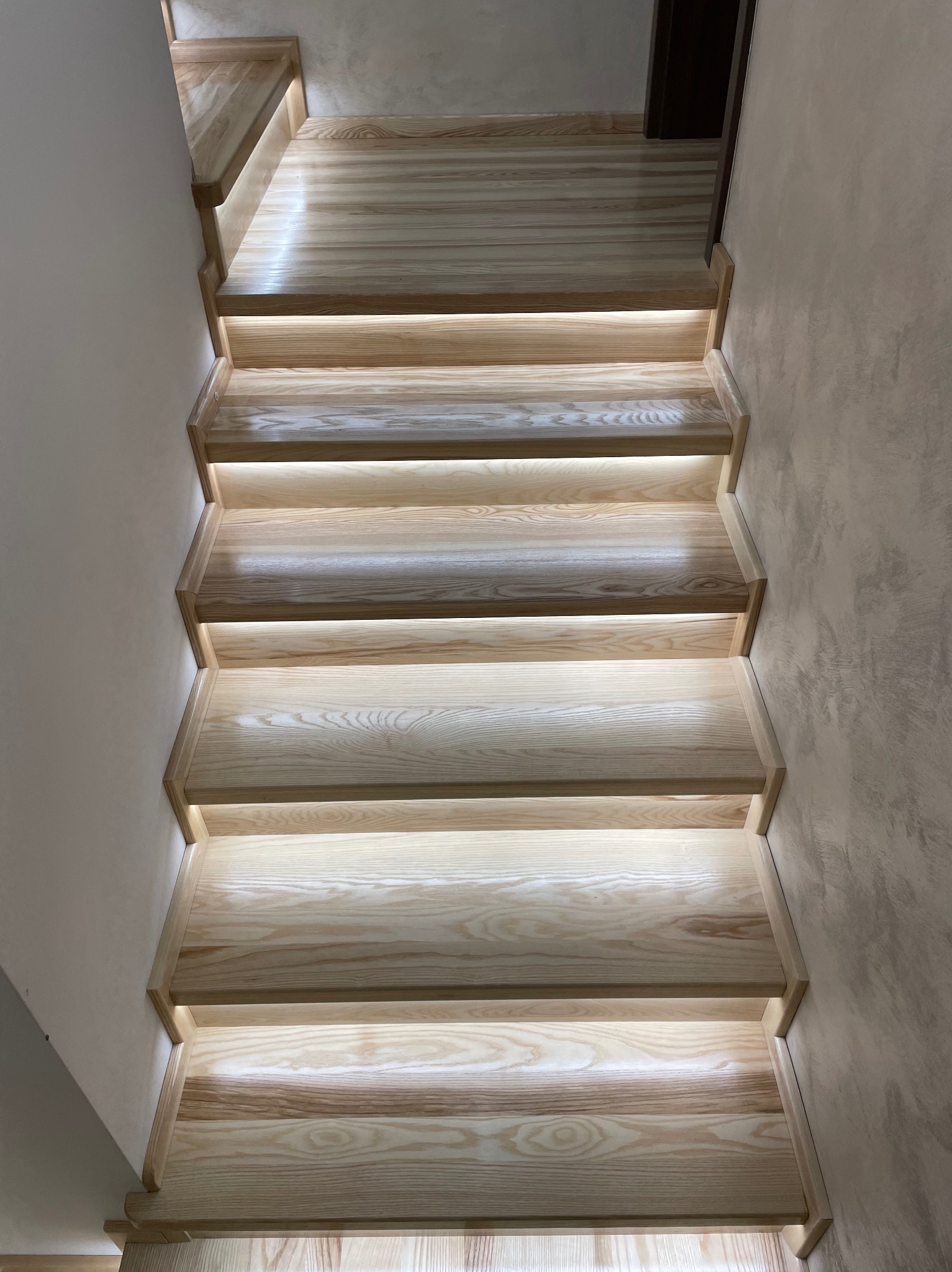 Drewniane schody z podświetleniem LED, widok z góry, ukazujące naturalne usłojenie drewna i nowoczesny design.