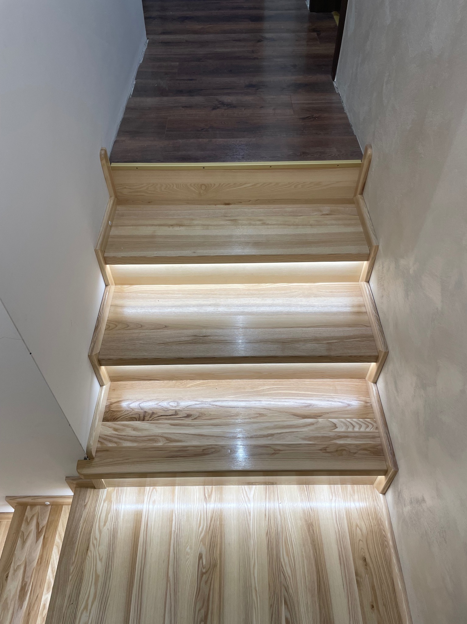 Jasne, drewniane schody z subtelnym oświetleniem LED pod stopniami, widok z góry, ukazujący naturalny rysunek drewna i minimalistyczny design.