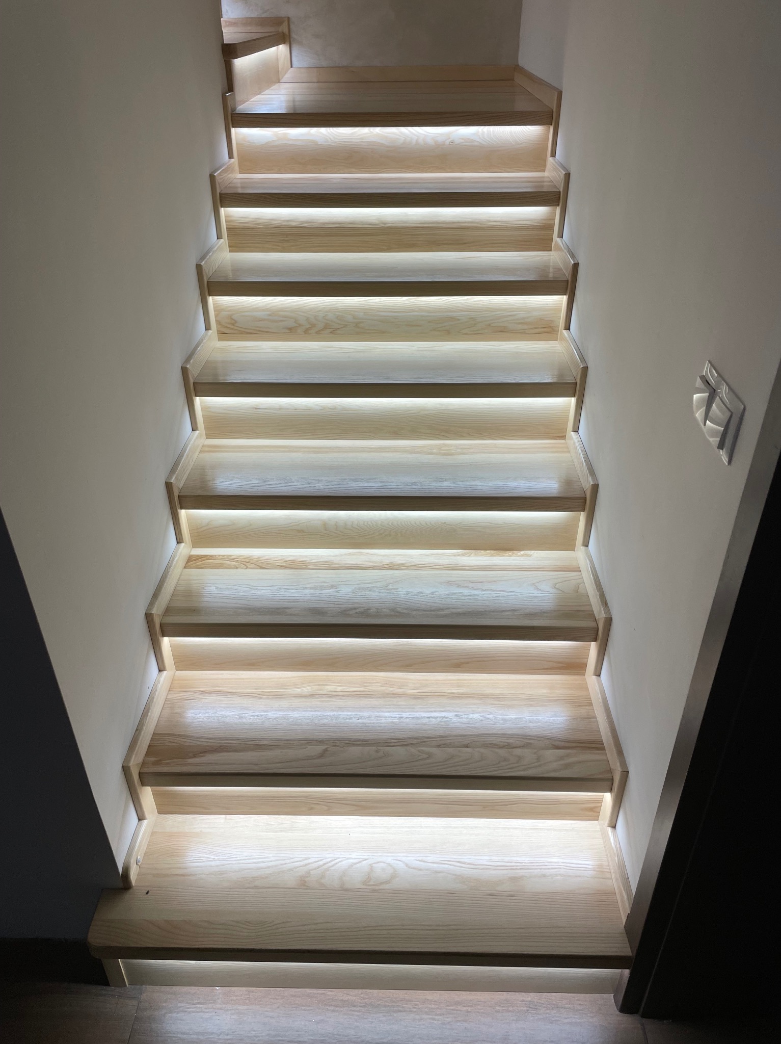 Drewniane schody z podświetleniem LED, widok z dołu. Jasne drewno, nowoczesny design, subtelne oświetlenie podkreśla strukturę stopni. Minimalistyczne wykończenie.