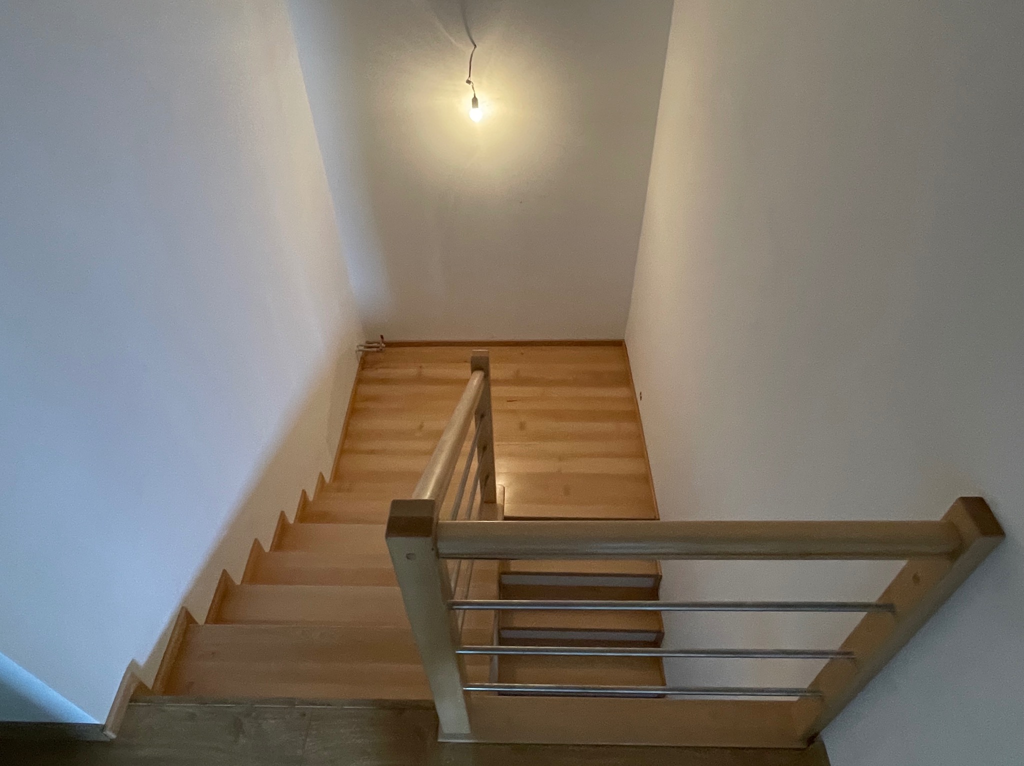 Jasne drewniane schody z metalową balustradą w nowym domu, widok z góry, oświetlone pojedynczą żarówką. Minimalistyczny design.