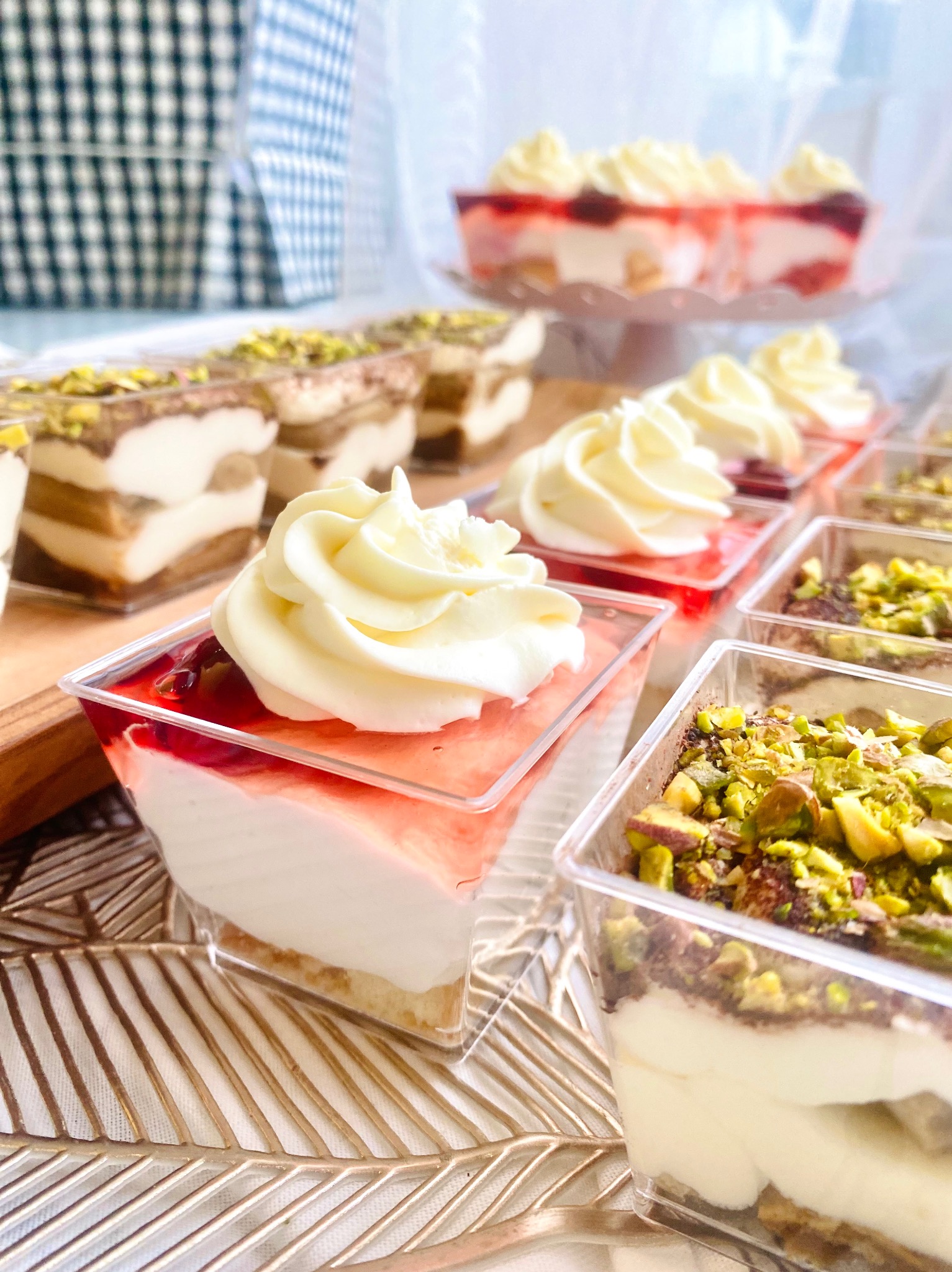 Deserki w przezroczystych pojemnikach: tiramisu z pistacjami, krem z owocami i bitą śmietaną. Różnorodność smaków na eleganckim przyjęciu.