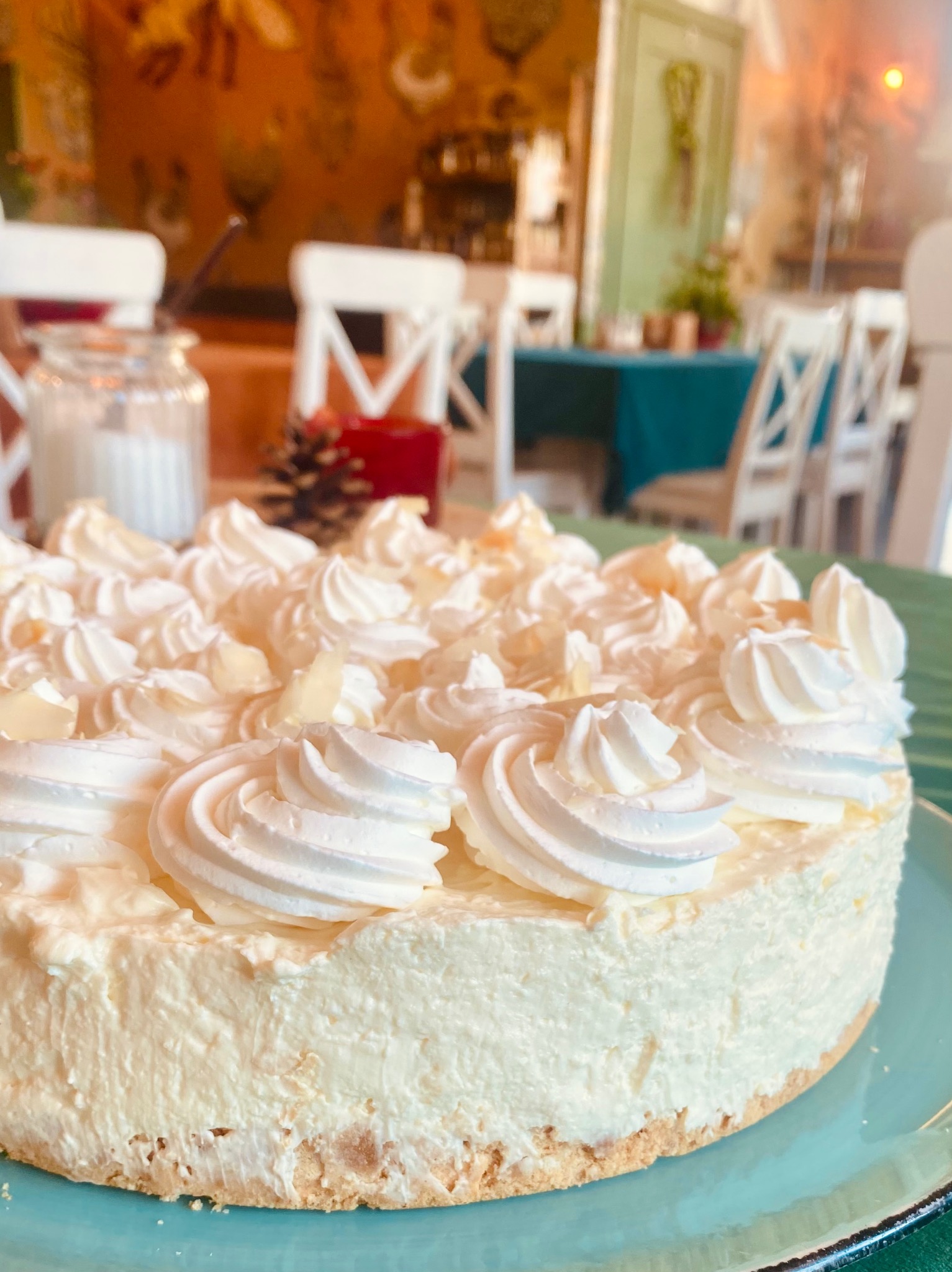 Tort z białym kremem i dekoracją z bitej śmietany na talerzu, w tle wystrój sali z białymi krzesłami i dekoracjami.