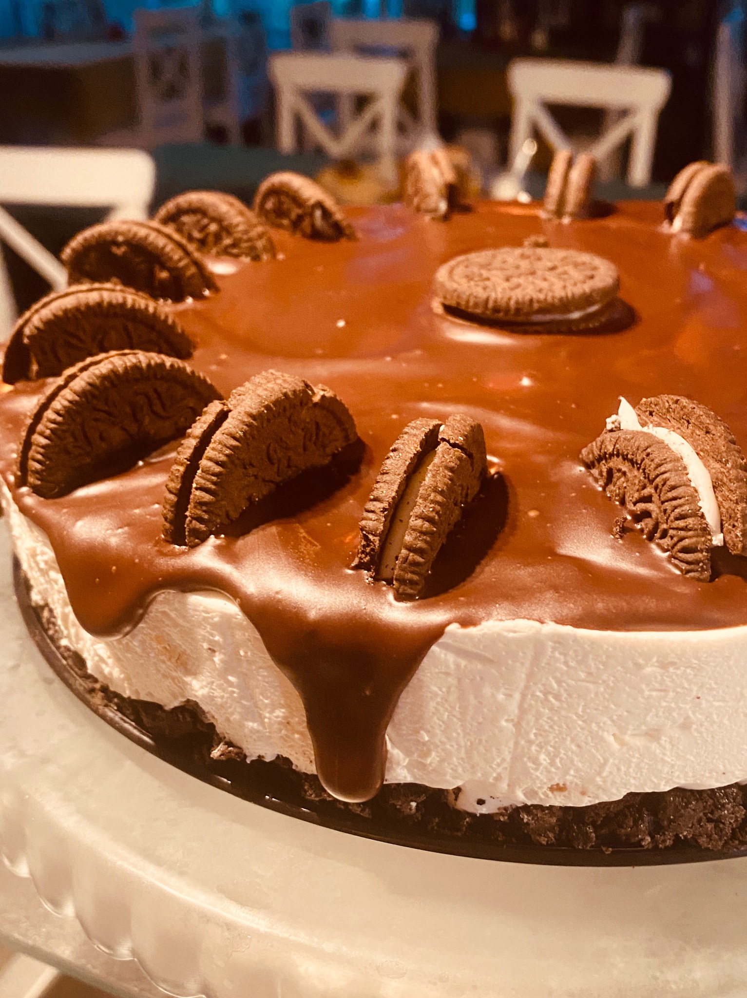 Apetyczny tort z polewą czekoladową i dekoracją z ciastek Oreo, prezentowany na jasnym tle, idealny na słodki poczęstunek.