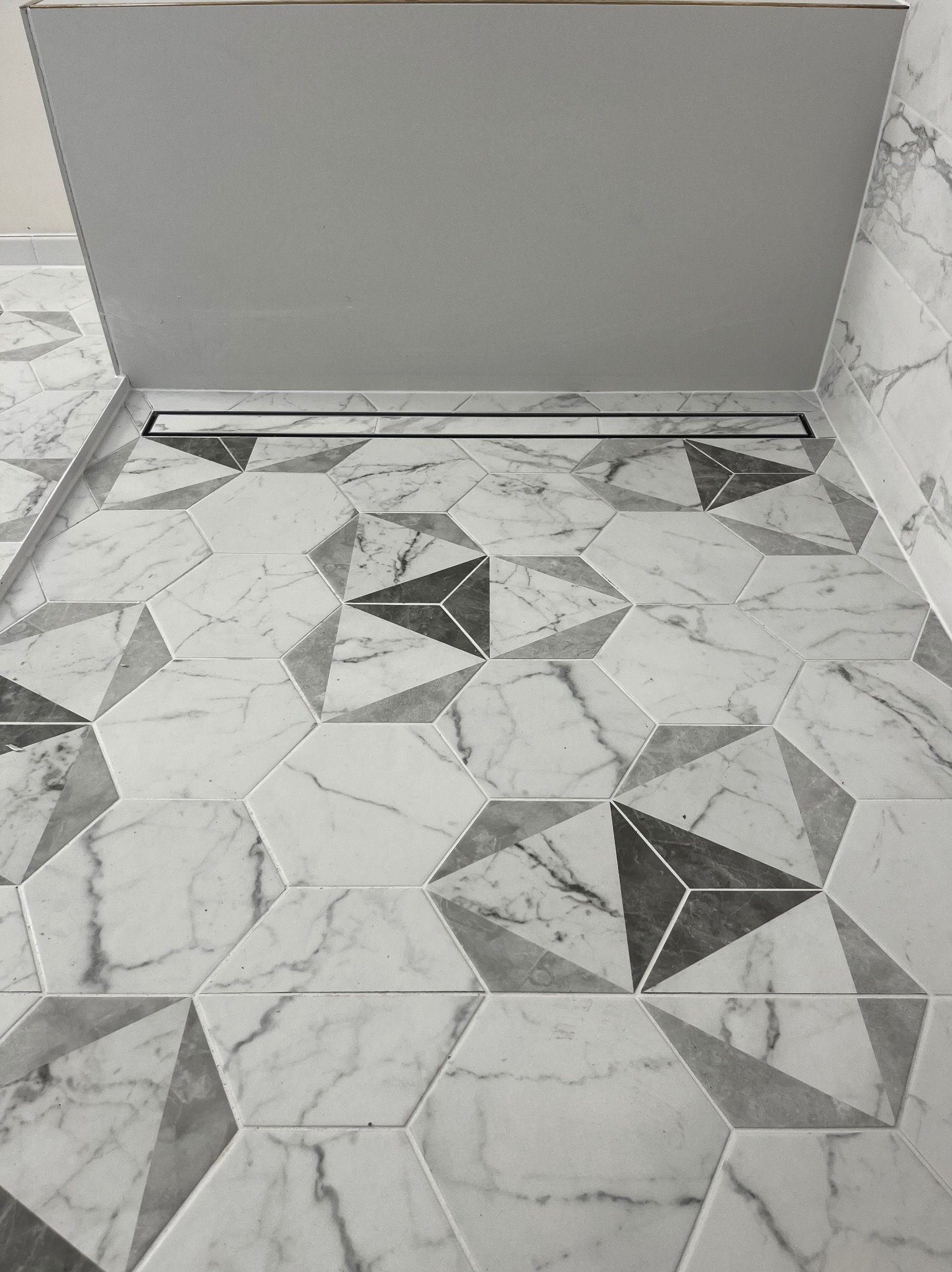 Wykończona podłoga w łazience z heksagonalnymi płytkami imitującymi marmur w odcieniach szarości i bieli. Widoczny liniowy odpływ.
