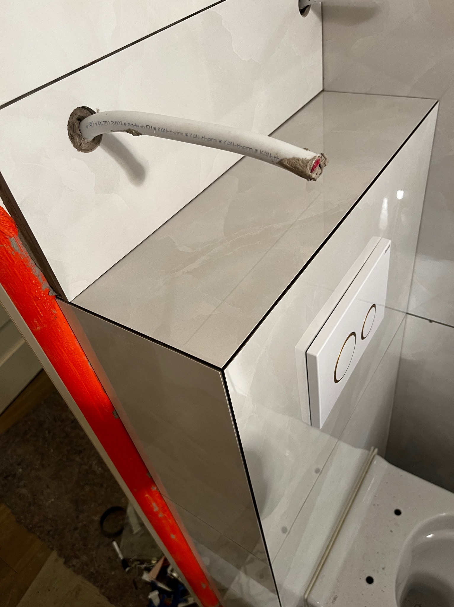 Świeżo ułożone płytki imitujące marmur w łazience, z widocznym fragmentem instalacji i przyciskiem spłuczki. Widoczna precyzja wykonania i dbałość o detale.