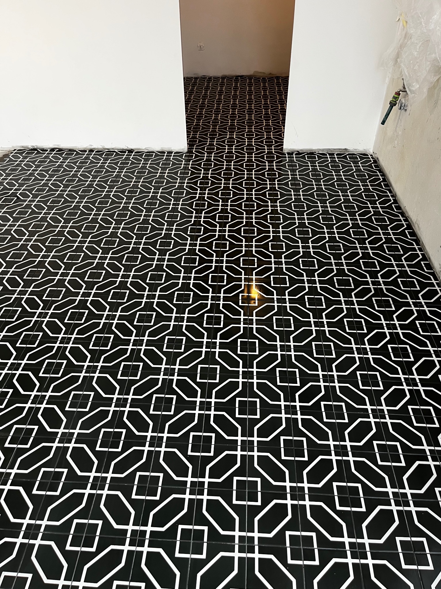 Nowoczesna, czarno-biała podłoga z płytek o geometrycznym wzorze, świeżo położona w jasnym pomieszczeniu. Fragment instalacji wodnej przy ścianie.