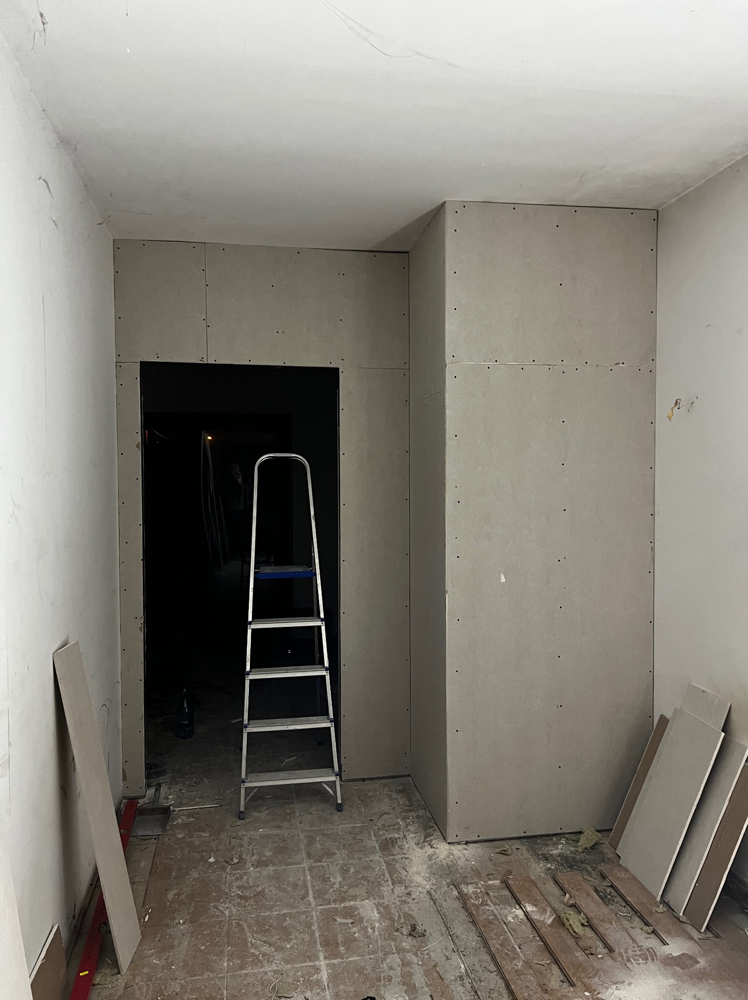 Montaż płyt G-K w Warszawie: Ściana działowa z otworem drzwiowym w trakcie budowy. Widoczna drabina i płyty. Surowy stan, przygotowanie do dalszych prac.