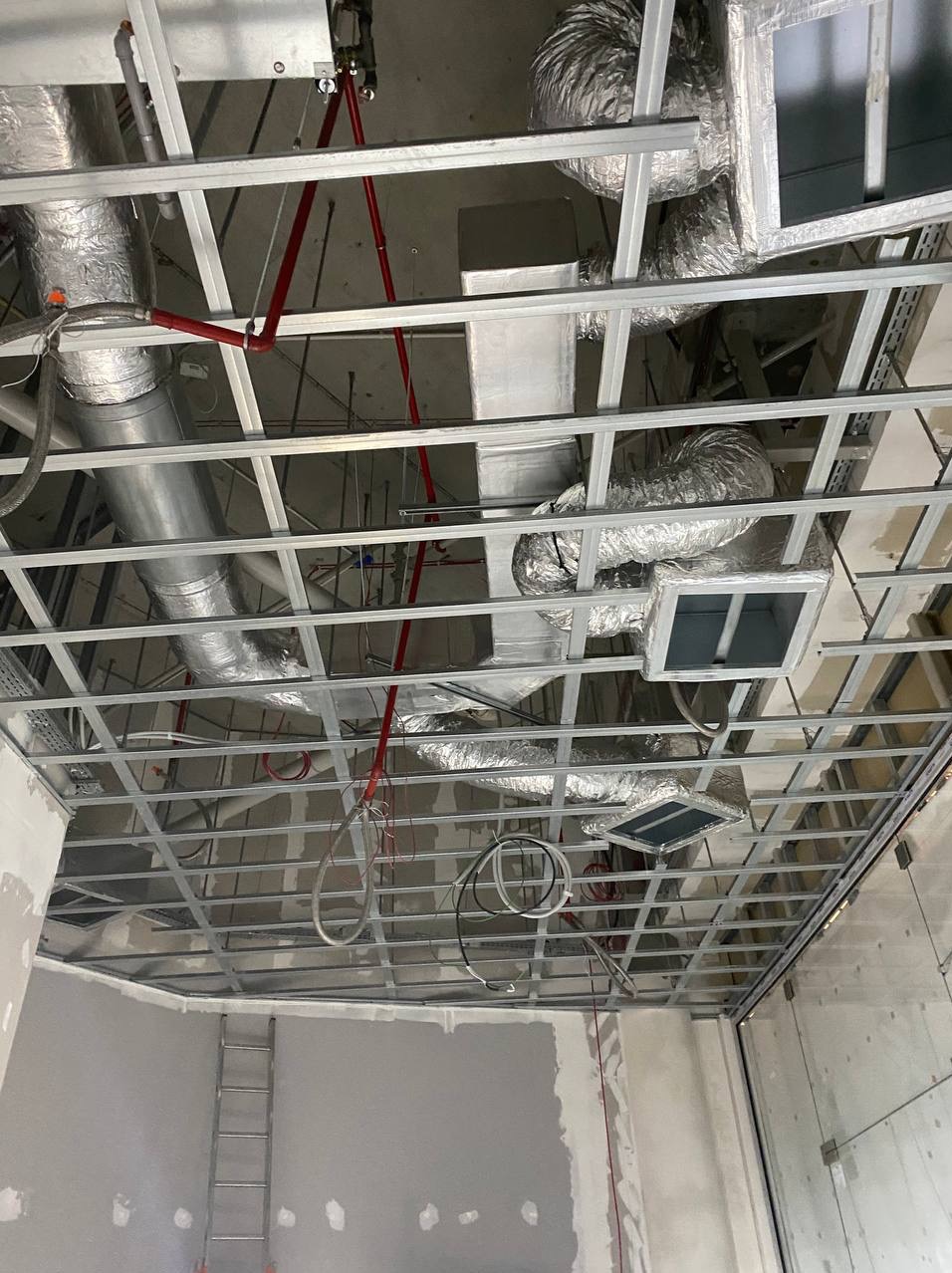 Sufit podwieszany z widoczną instalacją wentylacyjną i rurami, w trakcie montażu. Widoczne elementy konstrukcyjne i przewody wentylacyjne.
