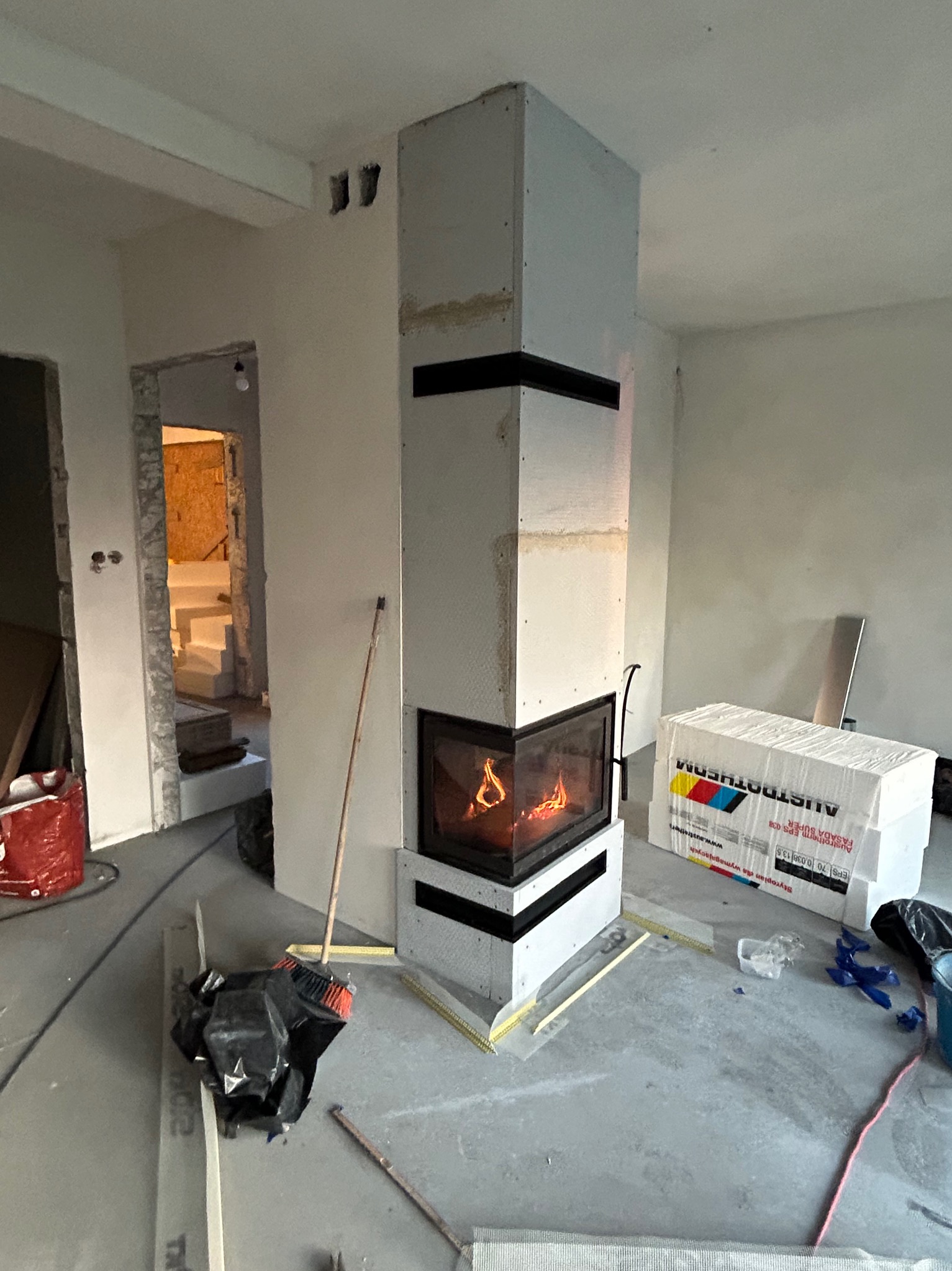 Wnętrze w Kamionce Wielkiej z kominkiem obudowanym płytami gipsowymi, w trakcie prac wykończeniowych. Widoczne materiały budowlane i narzędzia.