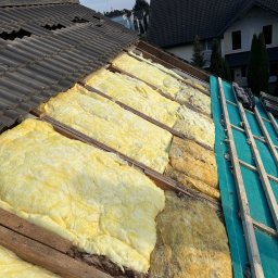 MajsterDACH - Odsłonięty dach z widoczną izolacją z wełny mineralnej i fragmentem nowej konstrukcji z zieloną membraną, ukazujący etap prac remontowych.
