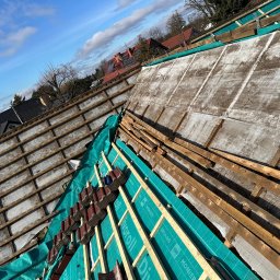 MajsterDACH - Dach w trakcie prac: widoczna konstrukcja, membrana w kolorze turkusowym z nadrukiem, częściowo ułożona dachówka. Słoneczny dzień, błękitne niebo z chmurami.