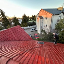 MajsterDACH - Czerwony dach z dachówki ceramicznej czyszczony myjką ciśnieniową przez dekarza. W tle budynek mieszkalny i drzewa w promieniach zachodzącego słońca.