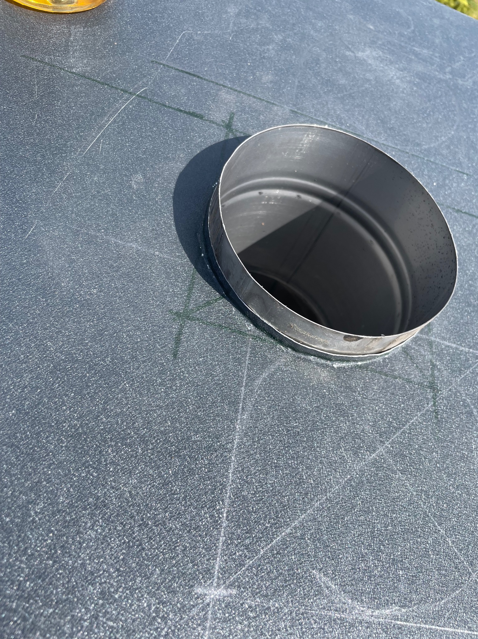 Fragment dachu z otworem i metalowym pierścieniem uszczelniającym komin. Widoczne ślady po cięciu na pokryciu dachowym.