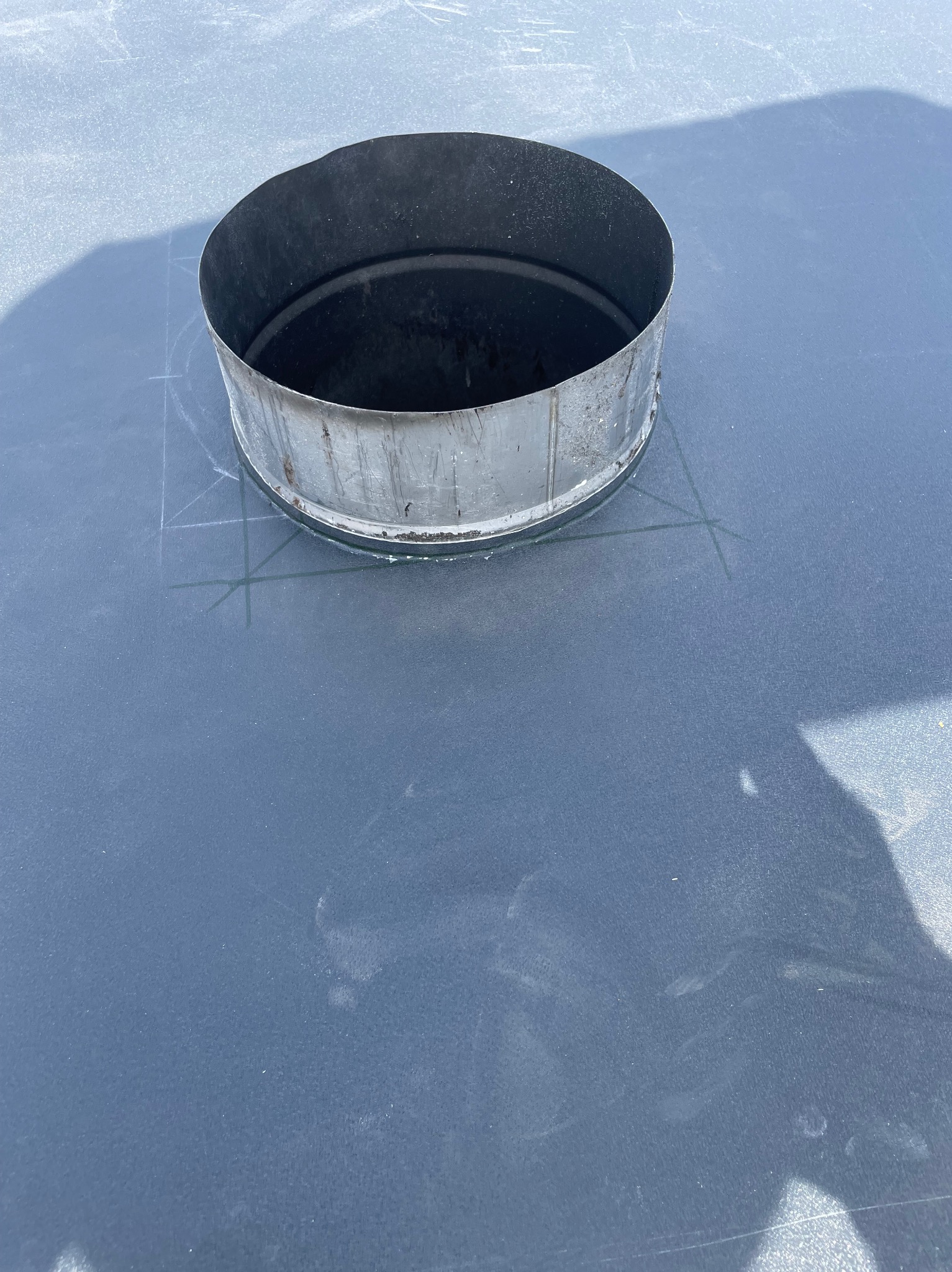 Metalowy komin na szarym dachu z widocznymi liniami pomocniczymi, przygotowany do montażu. Ujęcie z góry, oświetlenie dzienne.