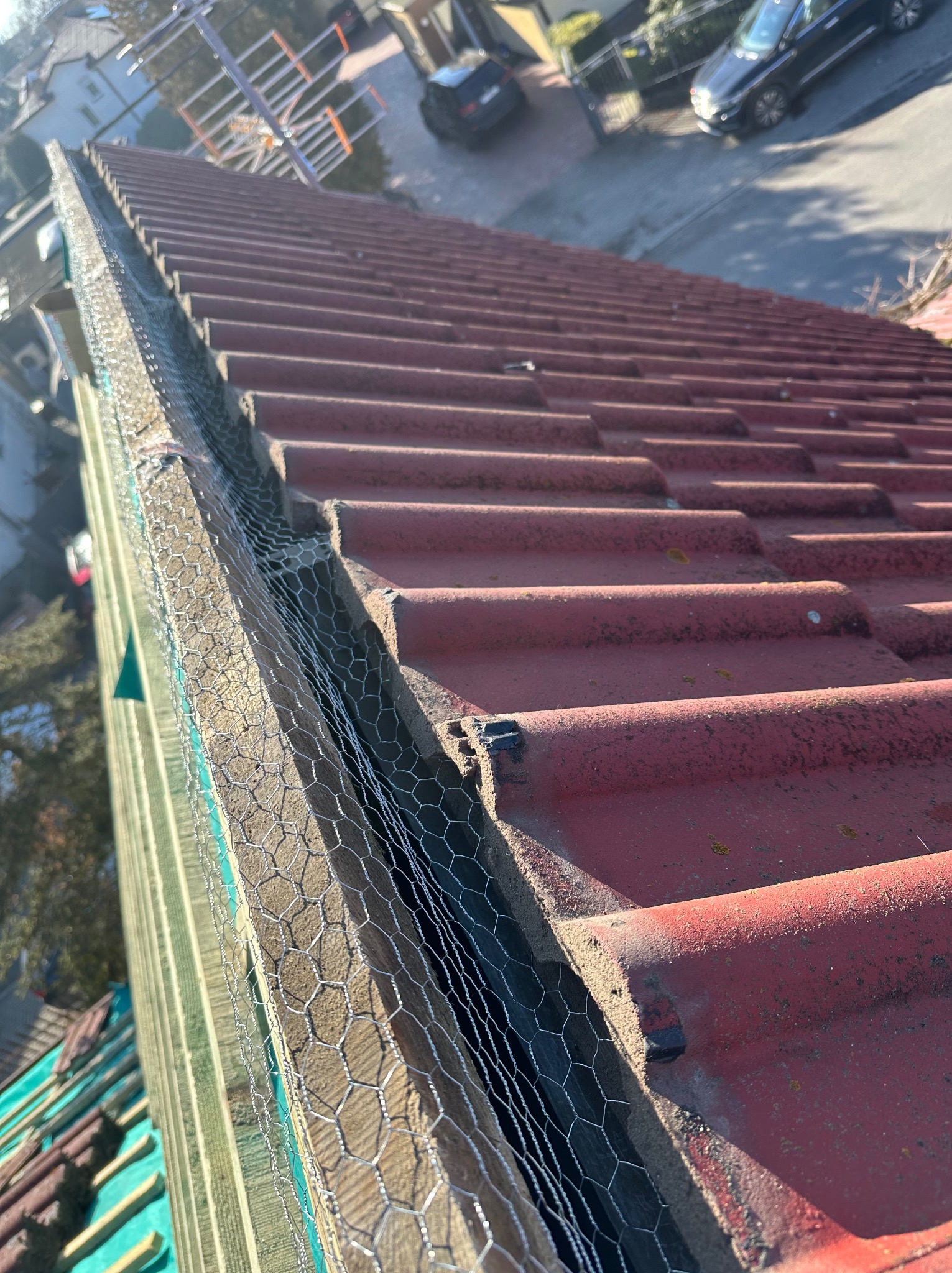 Czerwona dachówka z siatką zabezpieczającą przed ptakami i liśćmi, zamontowaną wzdłuż krawędzi dachu. Widok z góry, ukośny kadr.