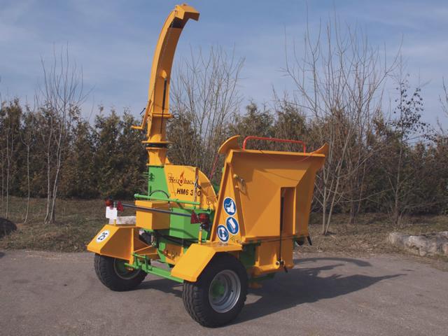 Żółto-zielony rębak Heizomat HM 6-300 na dwukołowym podwoziu, widoczne znaki ostrzegawcze.
