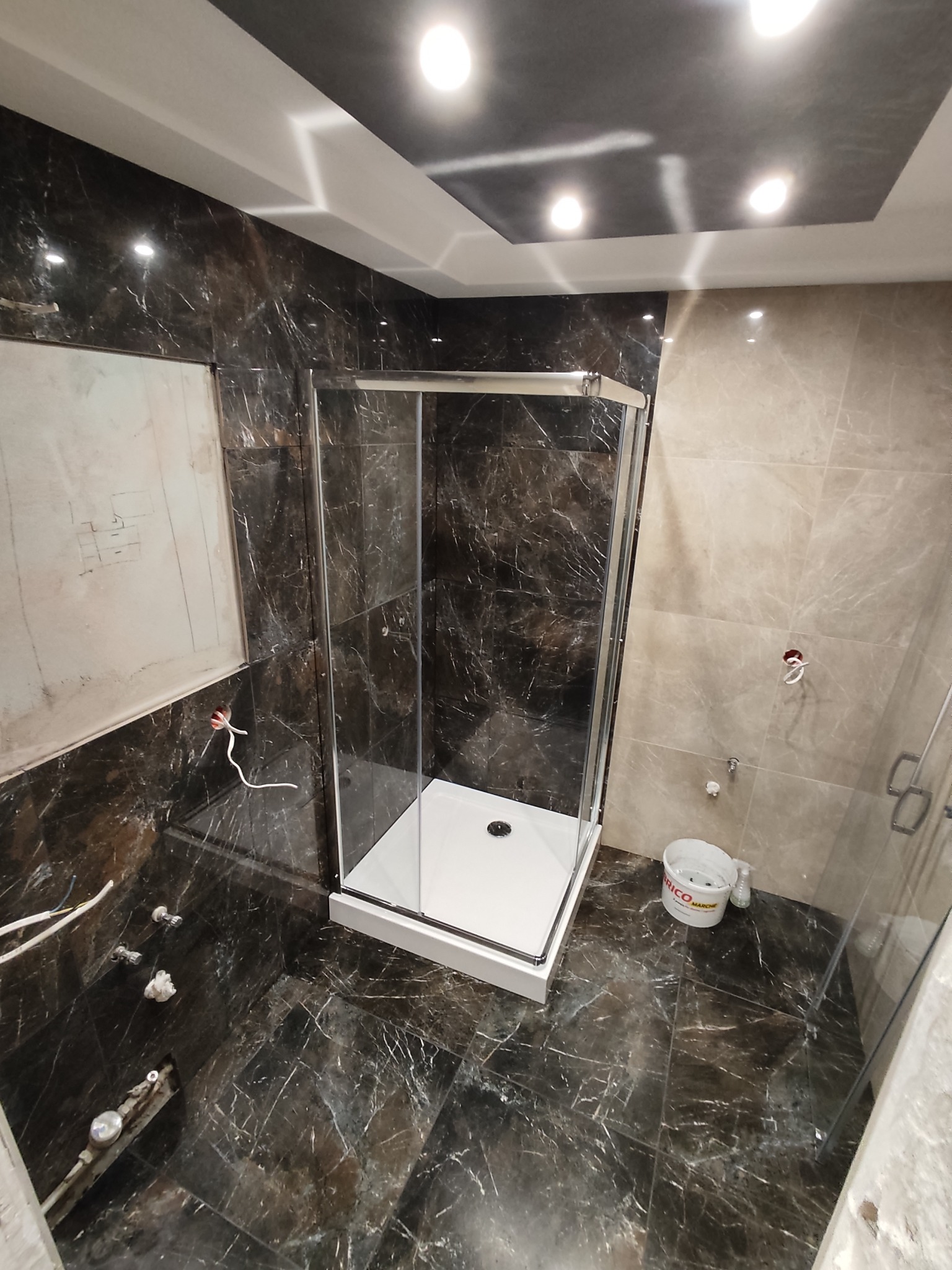 Montaż kabiny prysznicowej w łazience z marmurowymi płytkami w Międzyrzeczu. Widoczne przyłącza i narzędzia glazurnicze. Nowoczesny design.