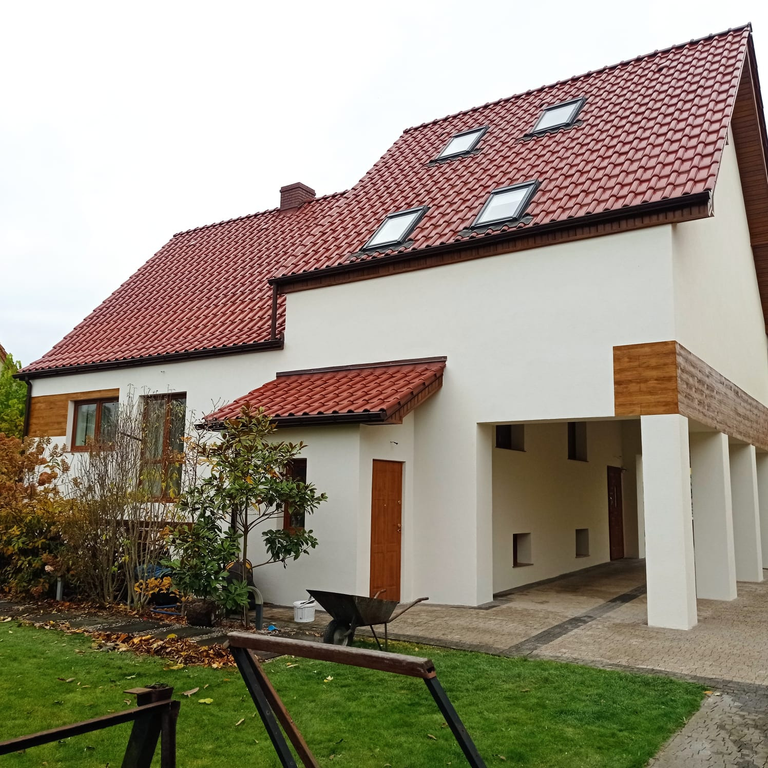 Dom jednorodzinny z czerwoną dachówką po renowacji elewacji, z widocznym podjazdem i fragmentem ogrodu. Uwagę zwraca jasna, odświeżona kolorystyka ścian.