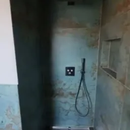 Kabina prysznicowa z deszczownicą i oryginalnymi płytkami w odcieniach turkusu i brązu. Widoczne półki w ścianie i nowoczesna armatura.