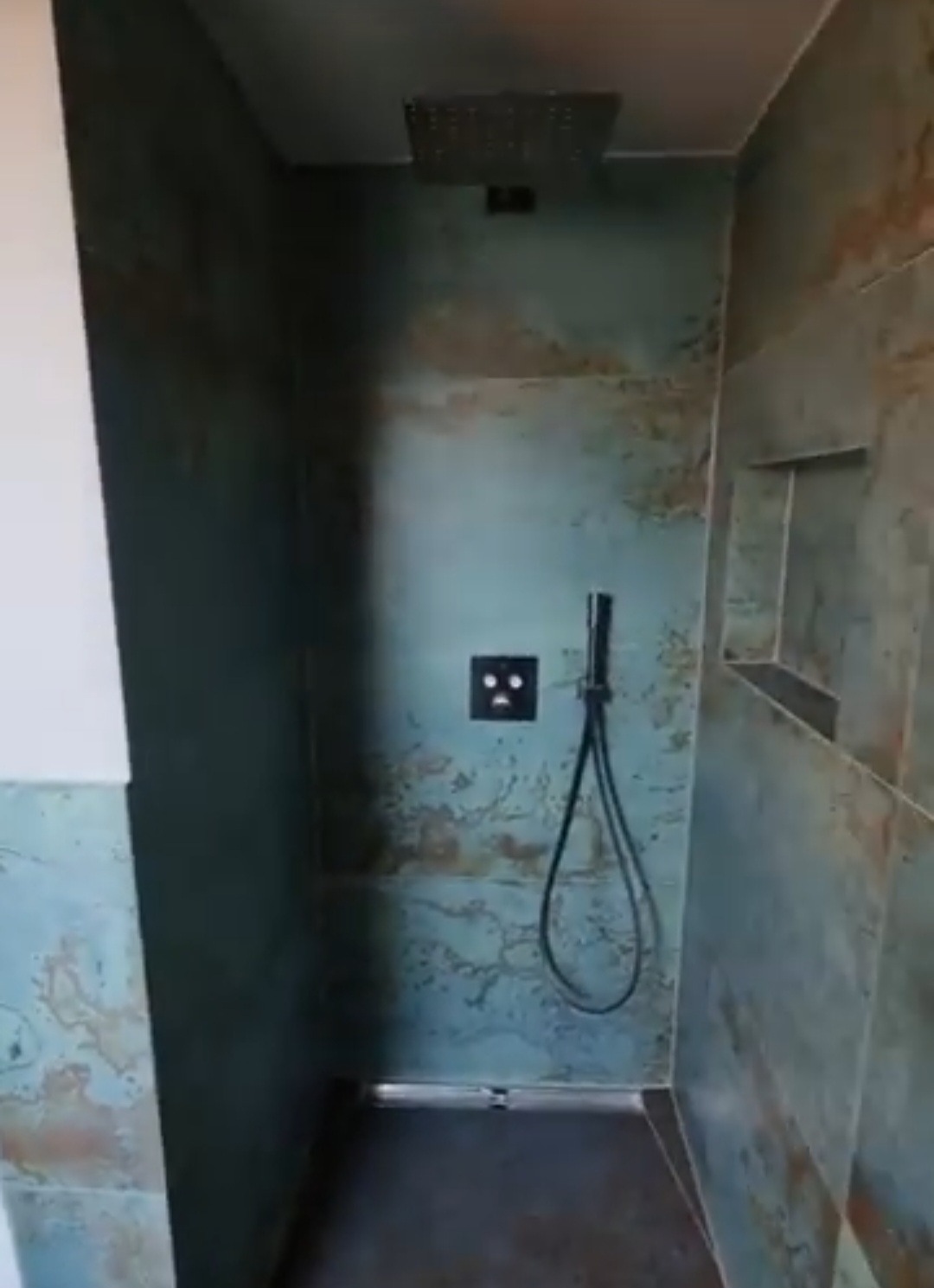 Kabina prysznicowa z deszczownicą i oryginalnymi płytkami w odcieniach turkusu i brązu. Widoczne półki w ścianie i nowoczesna armatura.