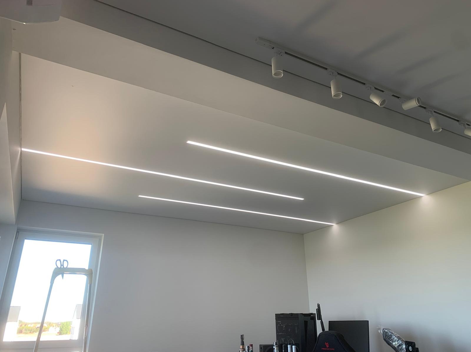 Nowoczesny sufit z liniowym oświetleniem LED, białe ściany, okno z drabiną. Minimalistyczny design wnętrza z elementami wyposażenia w tle.