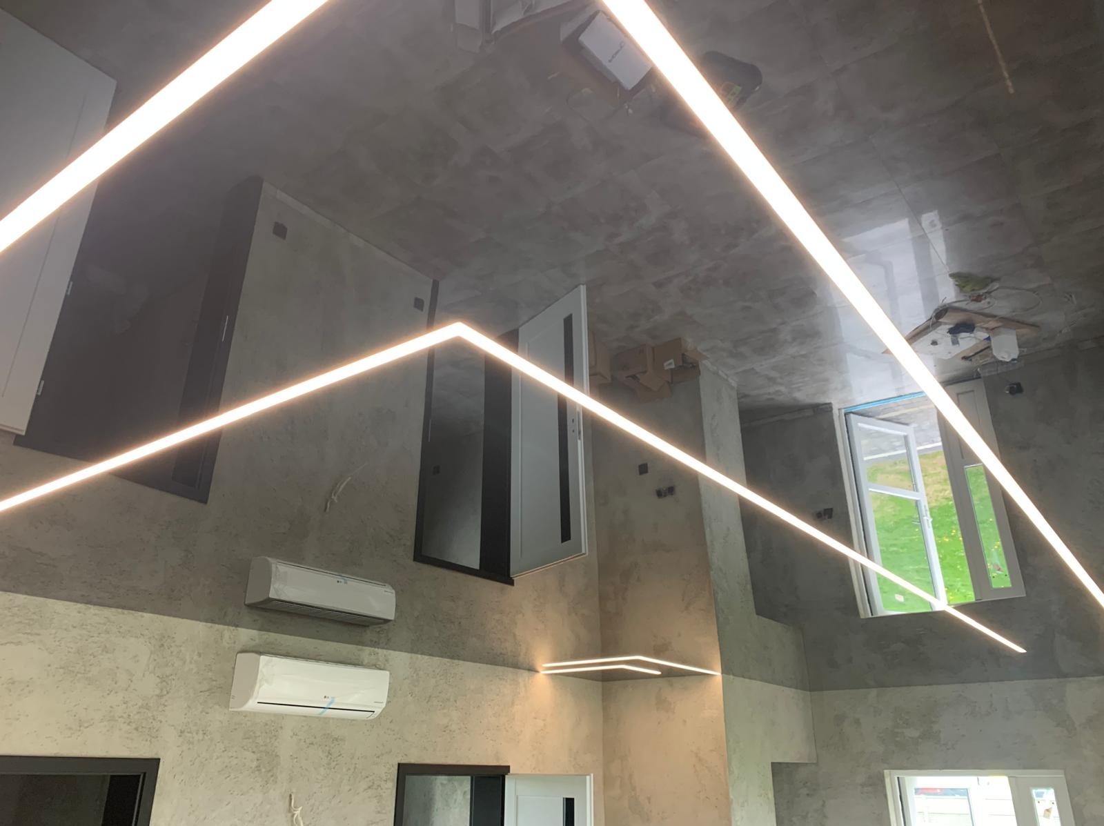 Wnętrze w trakcie wykańczania z liniowym oświetleniem LED na suficie i ścianach, widoczne okno, drzwi i klimatyzatory. Surowy beton na suficie dodaje industrialnego charakteru.