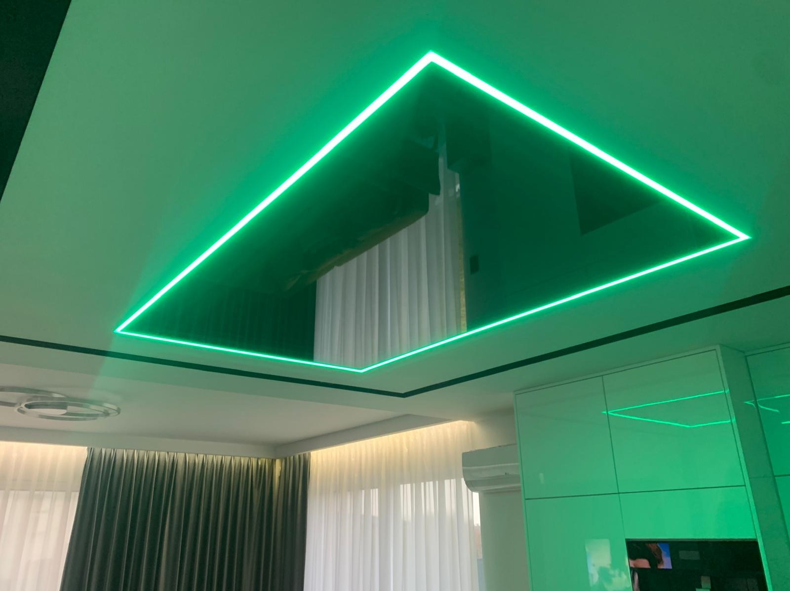 Błyszczący sufit napinany z podświetleniem LED tworzącym geometryczny wzór. Widoczne odbicie wnętrza w powierzchni sufitu.