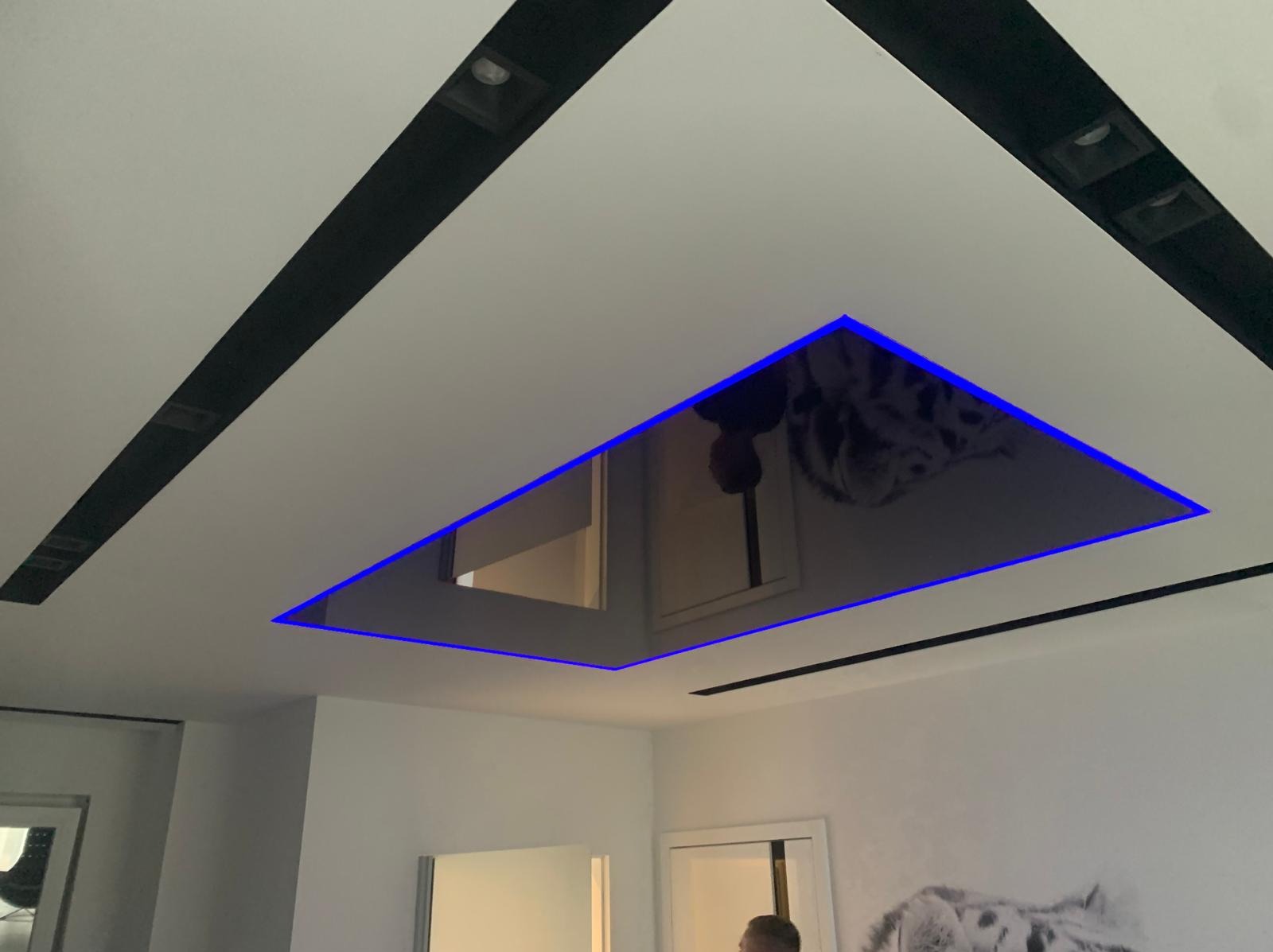 Nowoczesny sufit napinany z podświetleniem LED, tworzący iluzję lustra i odbijający fragment pomieszczenia, uzupełniony czarnymi listwami oświetleniowymi.