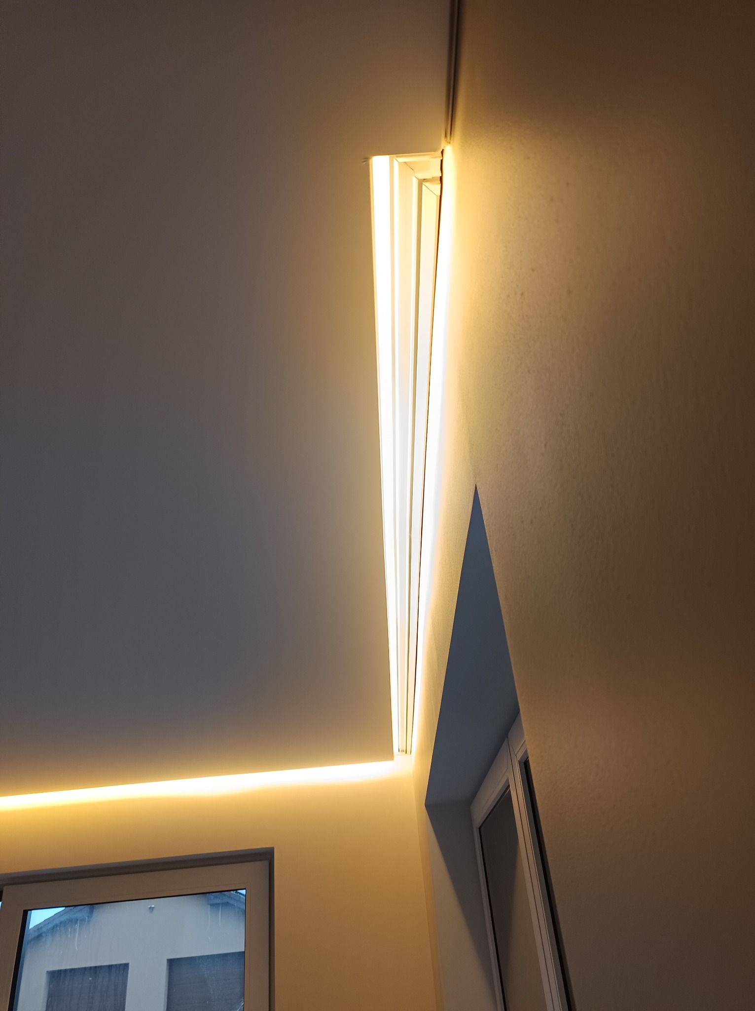 Nowoczesne oświetlenie LED w wykończonym wnętrzu: listwa sufitowa i podświetlenie nad oknem, ciepłe światło, gładkie ściany. Detal wykończenia.