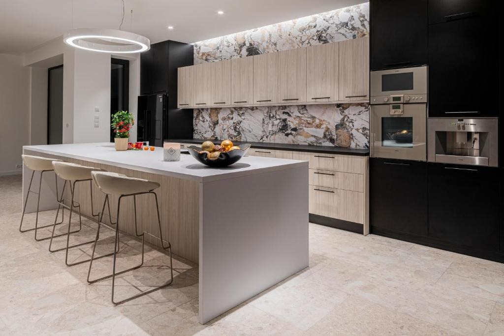 Nowoczesna kuchnia z wyspą, drewnianymi szafkami i marmurowym backsplashiem. Oświetlenie ledowe i minimalistyczne krzesła barowe.