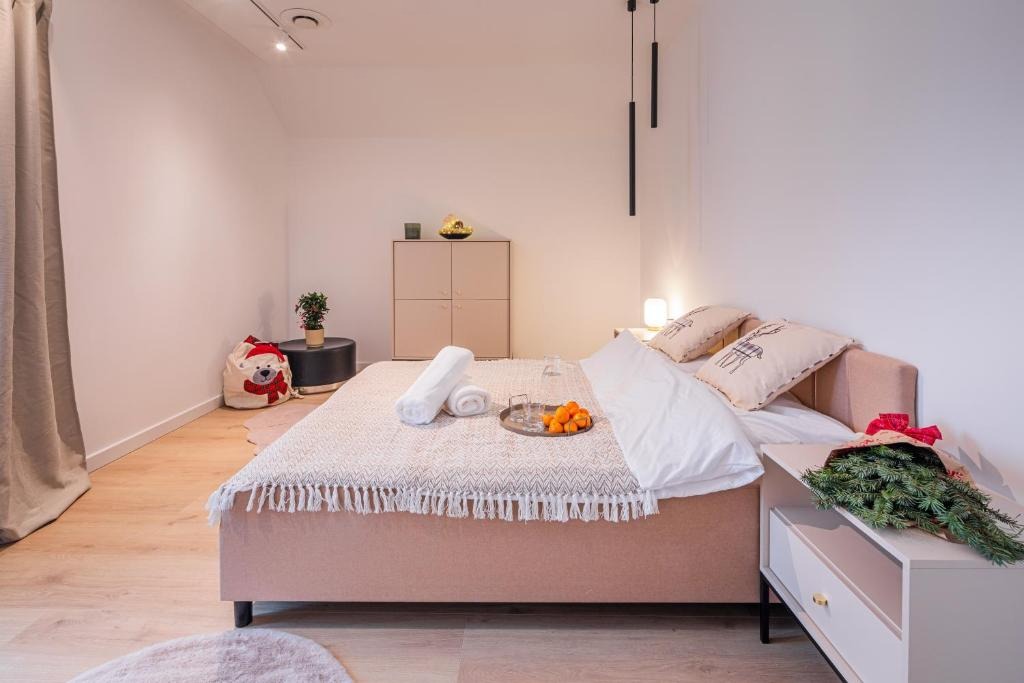 Jasny pokój z łóżkiem, na którym leżą ręczniki, owoce i szklanka. Na szafce bukiet z gałązek. W tle szafka i worek w kształcie misia. Przytulny klimat.