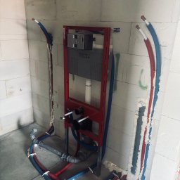 Hydro-klim - Stelaż WC TECE w czerwonej ramie, z podłączonymi rurami wodnymi w izolacji czerwono-niebieskiej, osadzony w surowej ścianie z betonu komórkowego.